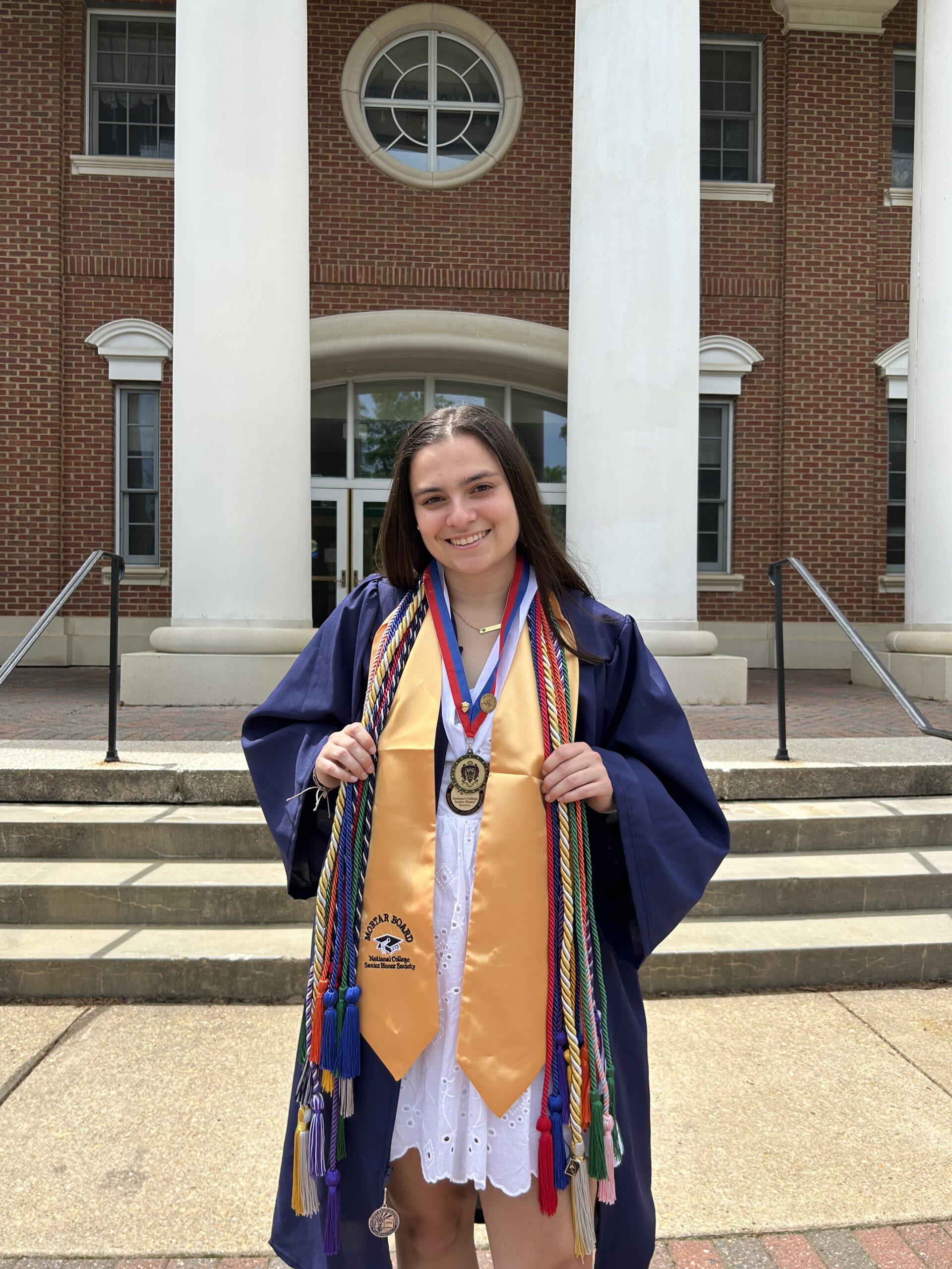 Senior Madeline Brunt poses in her graduation gown in front of the Jepson Science Center. Scholarships helped Madeline, who majored in biological sciences and minored in ethics, engage in undergraduate research, study abroad in the Galápagos Islands, and serve as president of UMW's Performing Arts Company. Photo courtesy of Madeline Brunt.