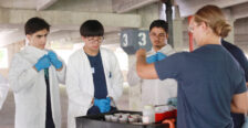 Hannah Steele '26, who earned a Noyce Scholarship at UMW, demonstrates to high schoolers Zubair Mohammadzai (left), Michael Young (center), and Maiwand Barakzai (right) how to soak the cotton balls in washable paint before throwing them at black canvases hanging in UMW's Alvey Parking Deck. Photo by K Pearlman Photography.