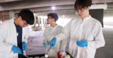 From left: High schoolers Michael Young, Alexander Rosas, and Vincent Phan dip cotton balls in washable paints before lobbing them at black canvases to create artwork resembling evolving stellar clusters, which they learned about in an astrophysics lesson. Photo by K Pearlman Photography.