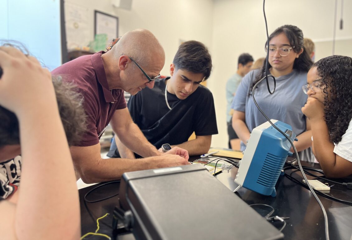 UMW Physics Chair and Professor Matt Fleenor demonstrates how to construct a circuit to high schooler Zubair Mohammadzai (center), while UMW student mentor Aliya Ather and volunteer mentor Emma Wallach (right) observe. Photo by Katie VanHouten '26.