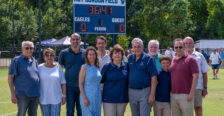 Coach Gordon poses with wife Terrie and their family in front of the scoreboard that overlooks the Roy Gordon Field. Photo by Kaitlynn Kimball.